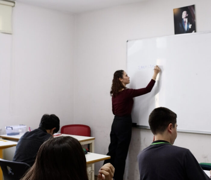 Öğretmen tahtada ders işlerken öğrenci parmak kaldırıyor